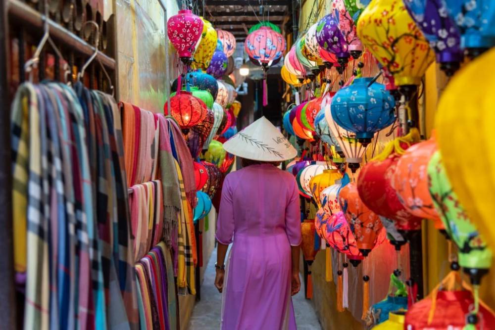 Une femme marche entre les stands de tissus et les lanternes à Hoi An